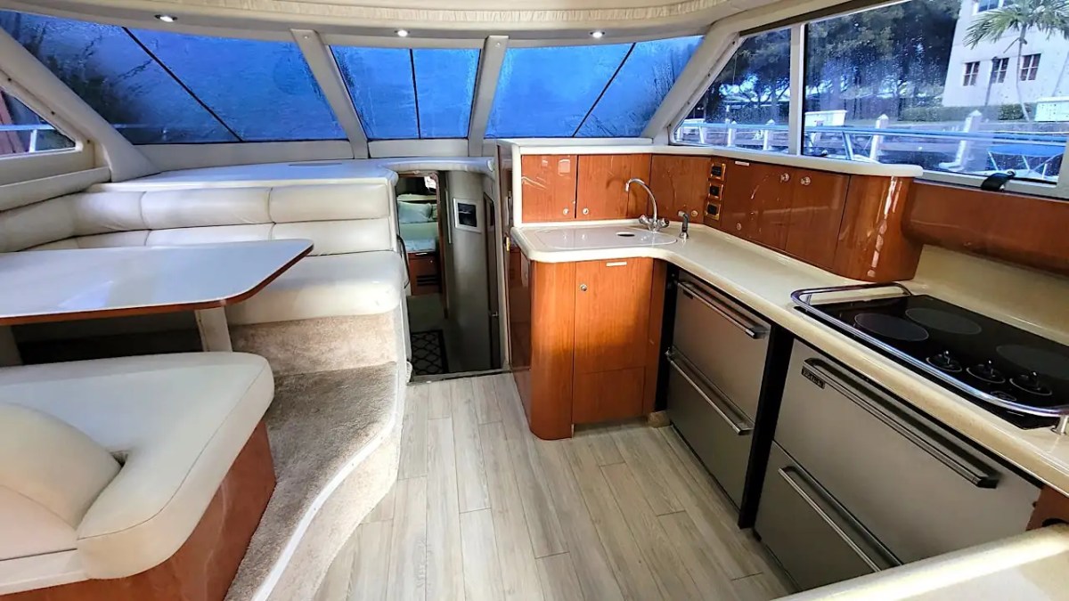 Interior of a yacht with a kitchenette and dining area, featuring wood cabinets and beige seating.