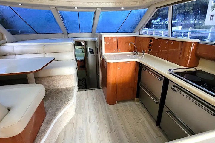 Interior of a yacht with a kitchenette and dining area, featuring wood cabinets and beige seating.