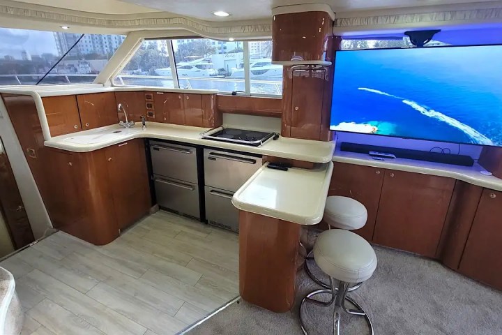 Luxury yacht interior with kitchen, stools, and large TV showing an ocean view.