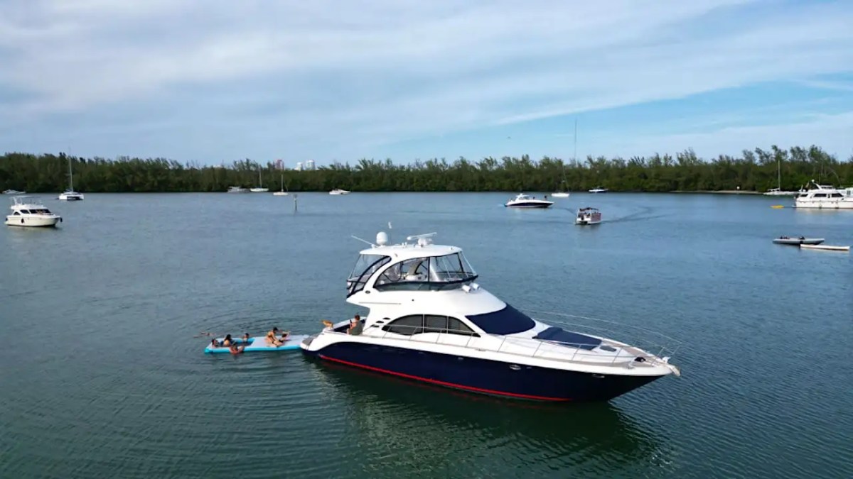 Yacht anchored in a bay with people on a float nearby, other boats in background.