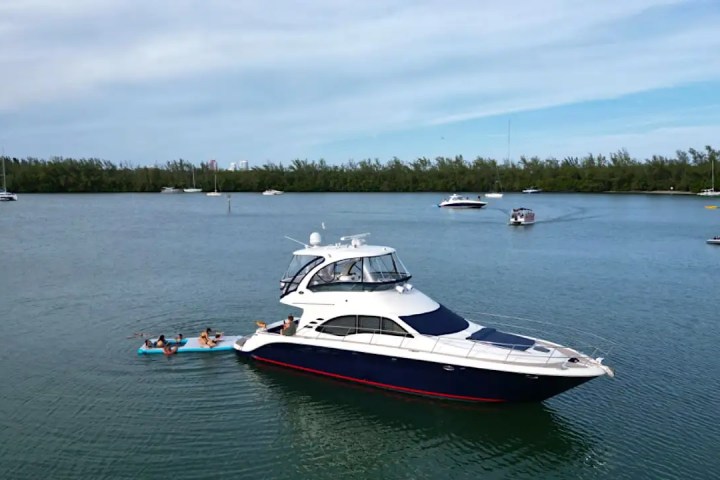 Yacht anchored in a bay with people on a float nearby, other boats in background.