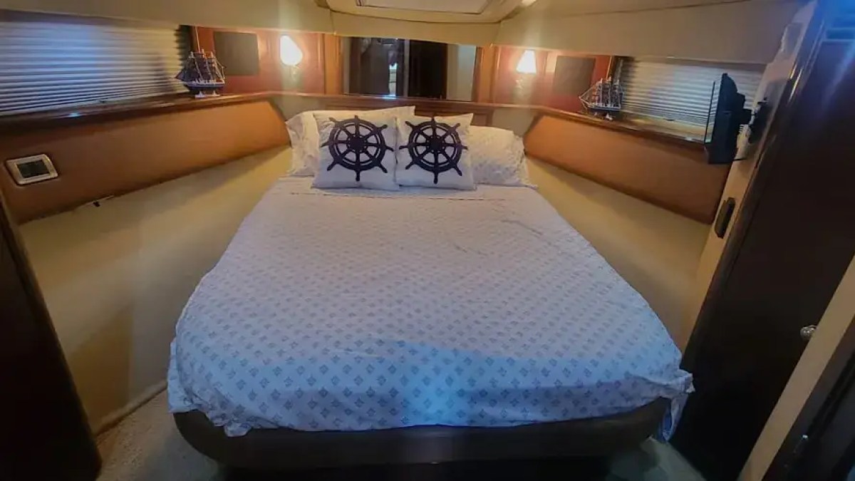Cozy boat cabin with bed, nautical-themed pillows, and decorative ship models on shelves.
