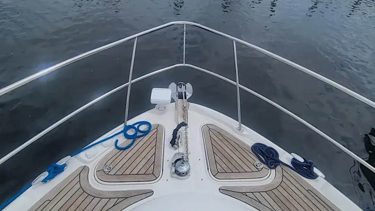 Boat bow with railing, ropes, and wood decking on calm water.