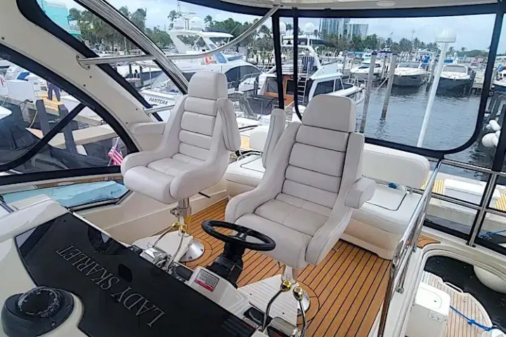 Interior of a yacht helm with two white captain chairs and view of marina.
