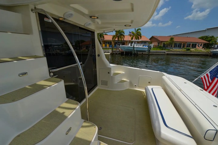 Boat deck with stairs, seating, and American flag in canalside setting with houses and palm trees.