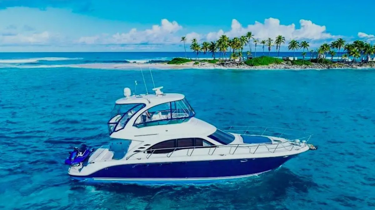 Luxury yacht on turquoise sea near a tropical island with palm trees.