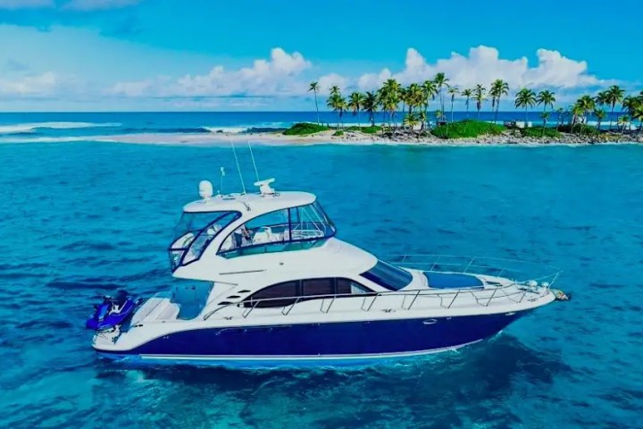 Luxury yacht on turquoise sea near a tropical island with palm trees.