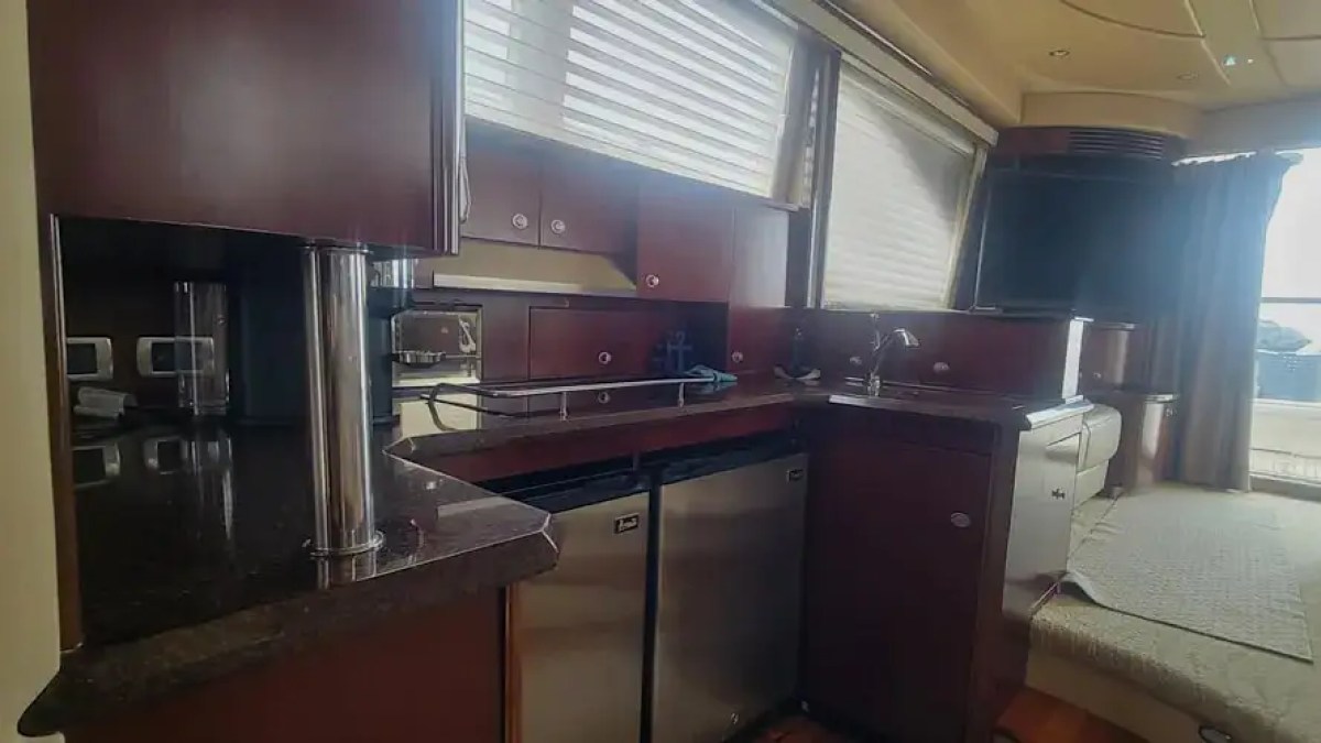 Luxurious yacht interior with kitchenette, dark wood cabinets, sofa, and large windows.