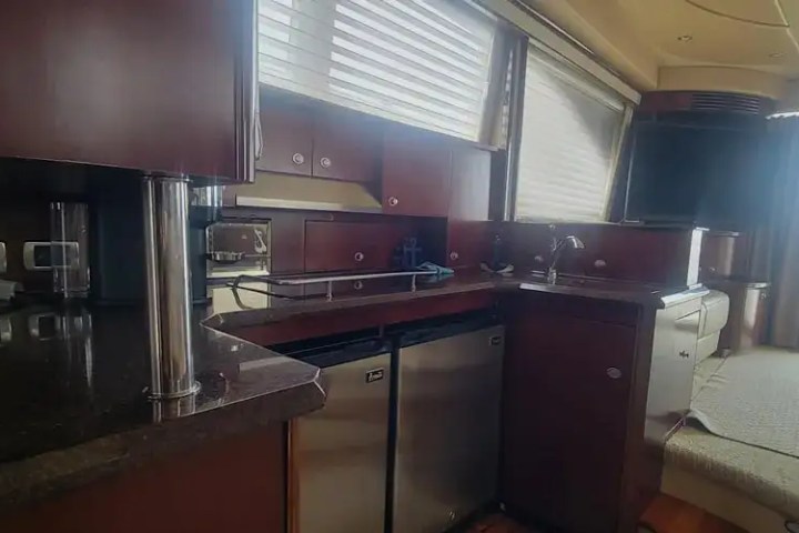 Luxurious yacht interior with kitchenette, dark wood cabinets, sofa, and large windows.