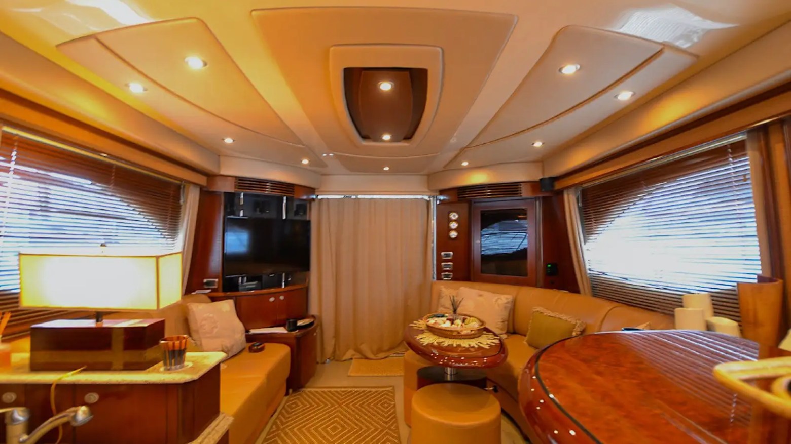 Luxurious yacht interior with seating, table, and mood lighting, featuring wood finishes and blinds on windows.