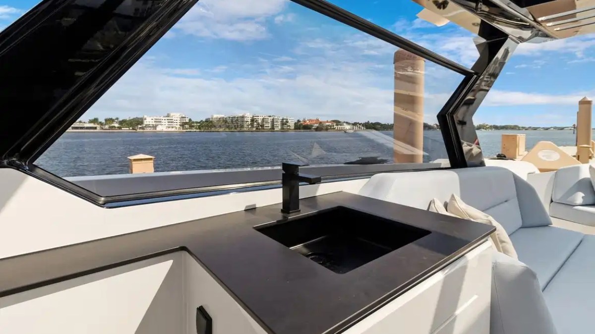 Boat interior with sink, sofa, and lake view through large windows.