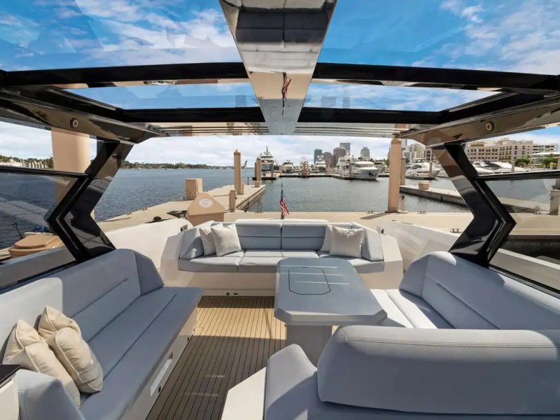 Luxury yacht deck with sofas and table, overlooking a marina with city skyline.