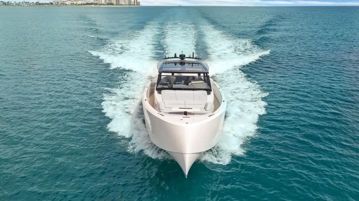 A sleek yacht speeding across blue waters with a city skyline in the background.
