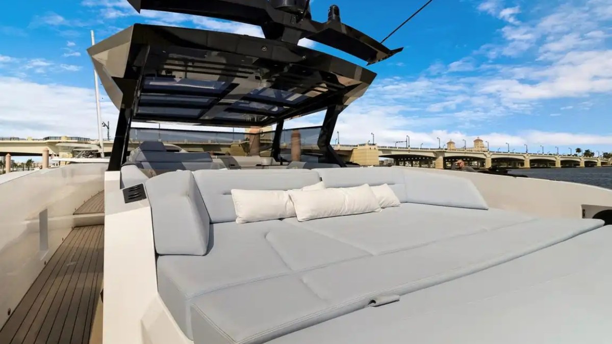 Modern yacht deck with sun lounge, black canopy, and bridge in background, under blue sky.
