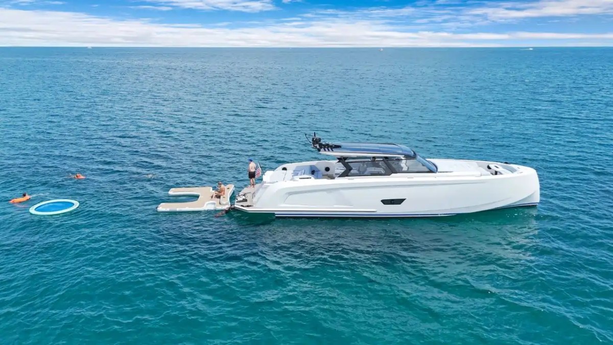 White yacht on the ocean with people swimming and a floating ring nearby.