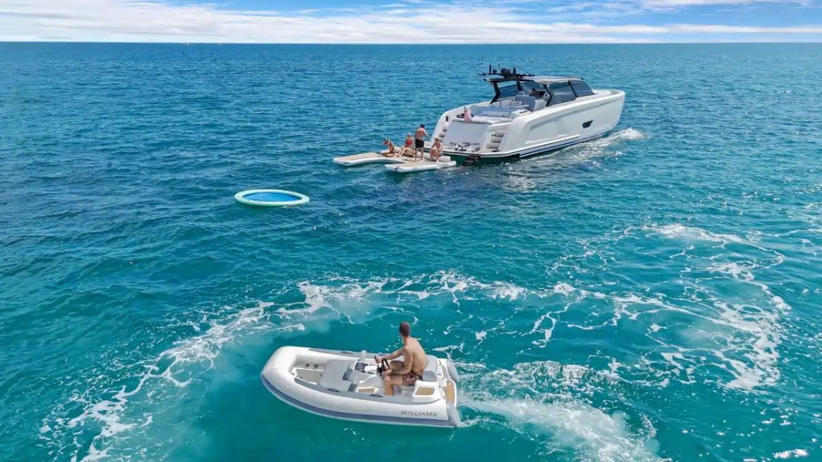 Two boats on open water; a person rides a small boat approaching a larger boat with people on deck.