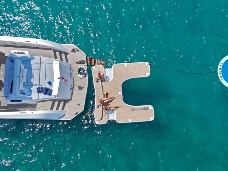 Aerial view of yacht, floating deck, and circular water platform on turquoise sea.