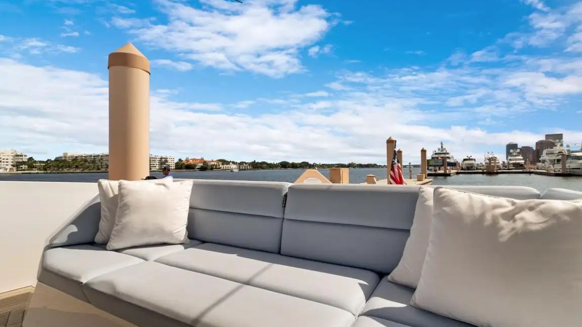 Outdoor couch on a boat with city skyline and harbor in background under blue sky.