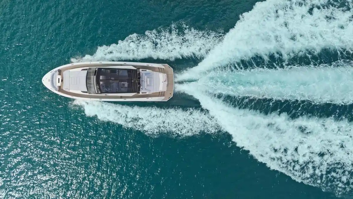 Aerial view of a yacht cruising on clear blue water leaving a wake behind.