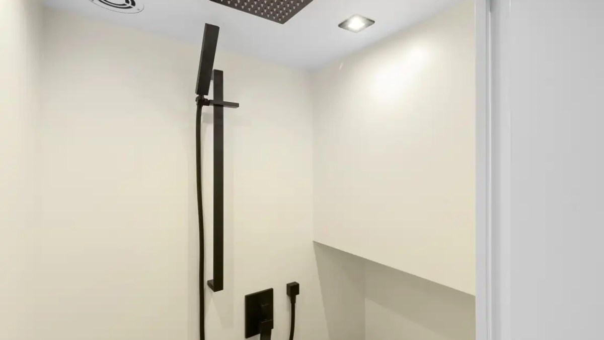Minimalist shower with black fixtures, rainfall showerhead, and white walls.