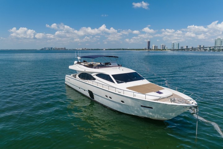 White yacht sailing on blue water with city skyline in the background.