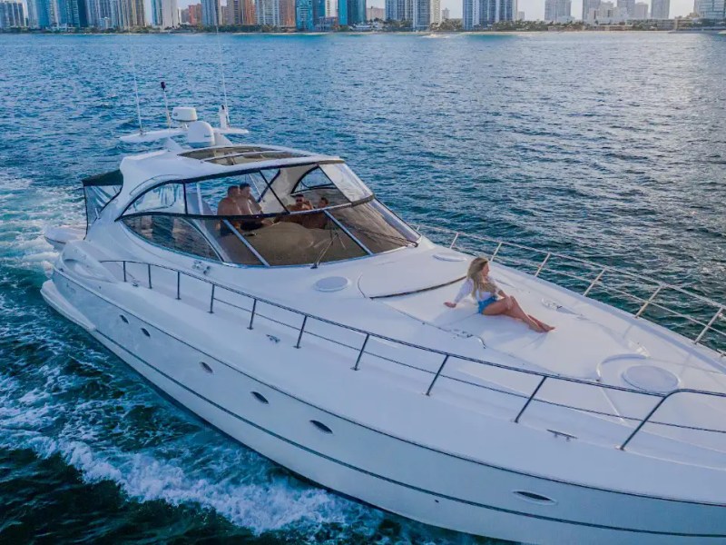 Luxury yacht on water with a person lounging on the deck, city skyline in the background.