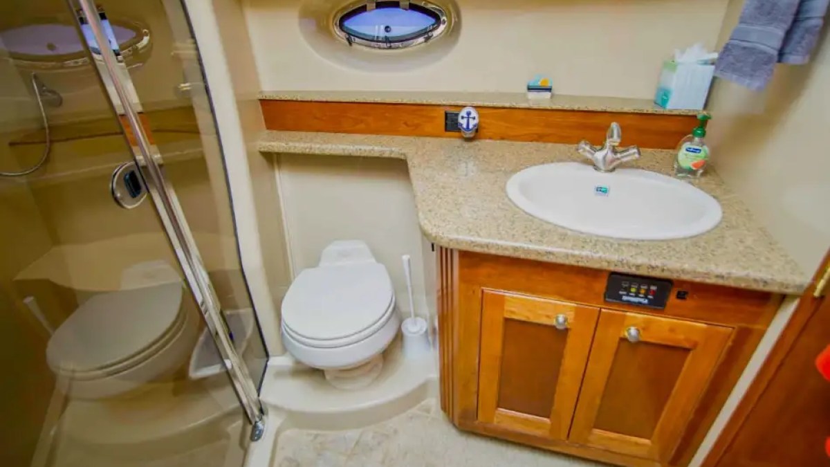 Compact bathroom with a shower, toilet, sink, and wooden cabinet.
