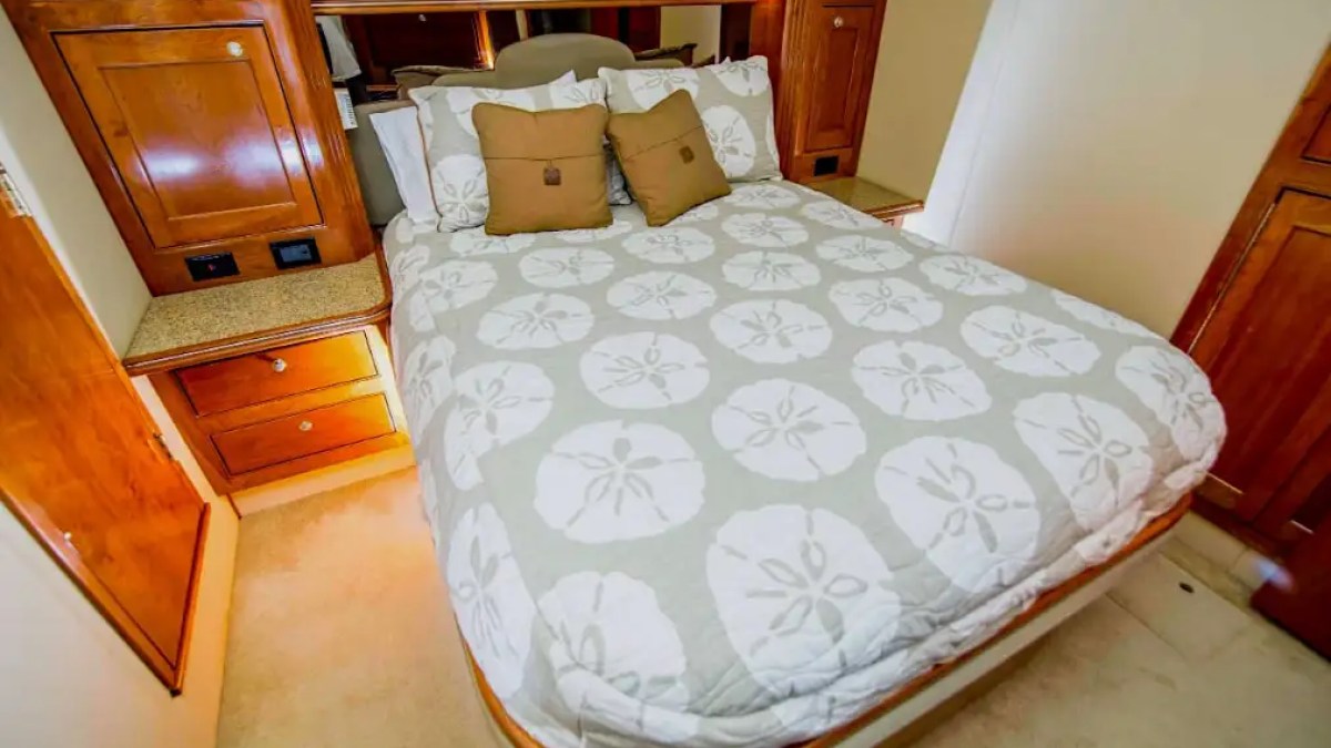 Cozy boat cabin with bed, sand dollar duvet, and wooden cabinetry.