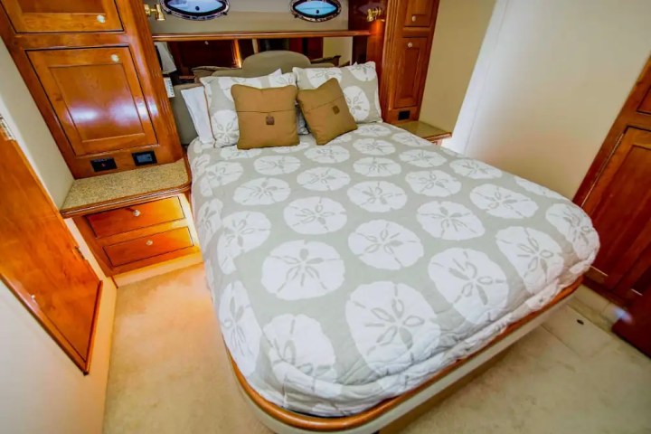 Cozy boat cabin with bed, sand dollar duvet, and wooden cabinetry.