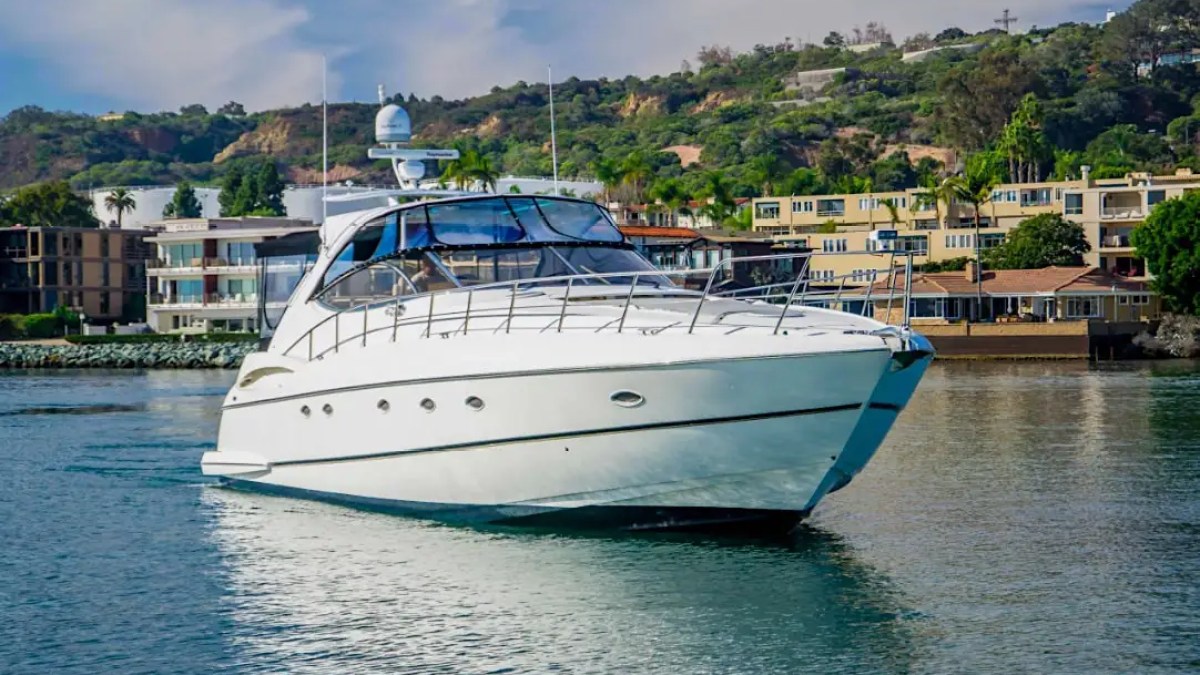 White yacht on calm water with hillside and houses in the background.