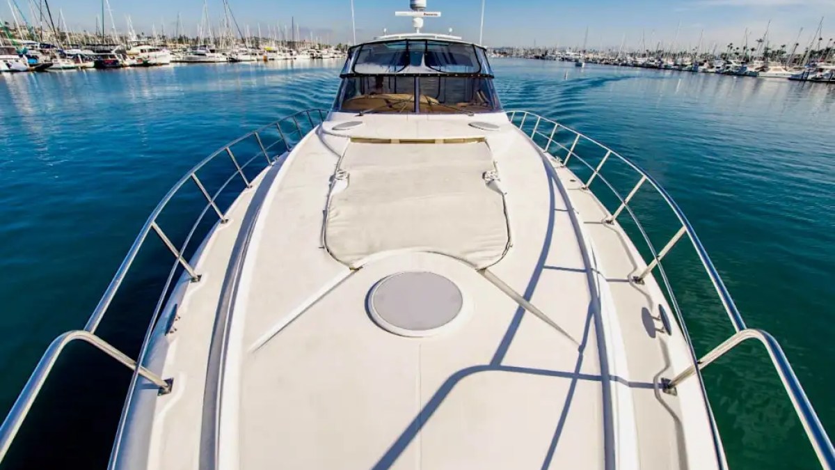 Bow of a yacht in harbor with clear blue water and numerous docked boats.