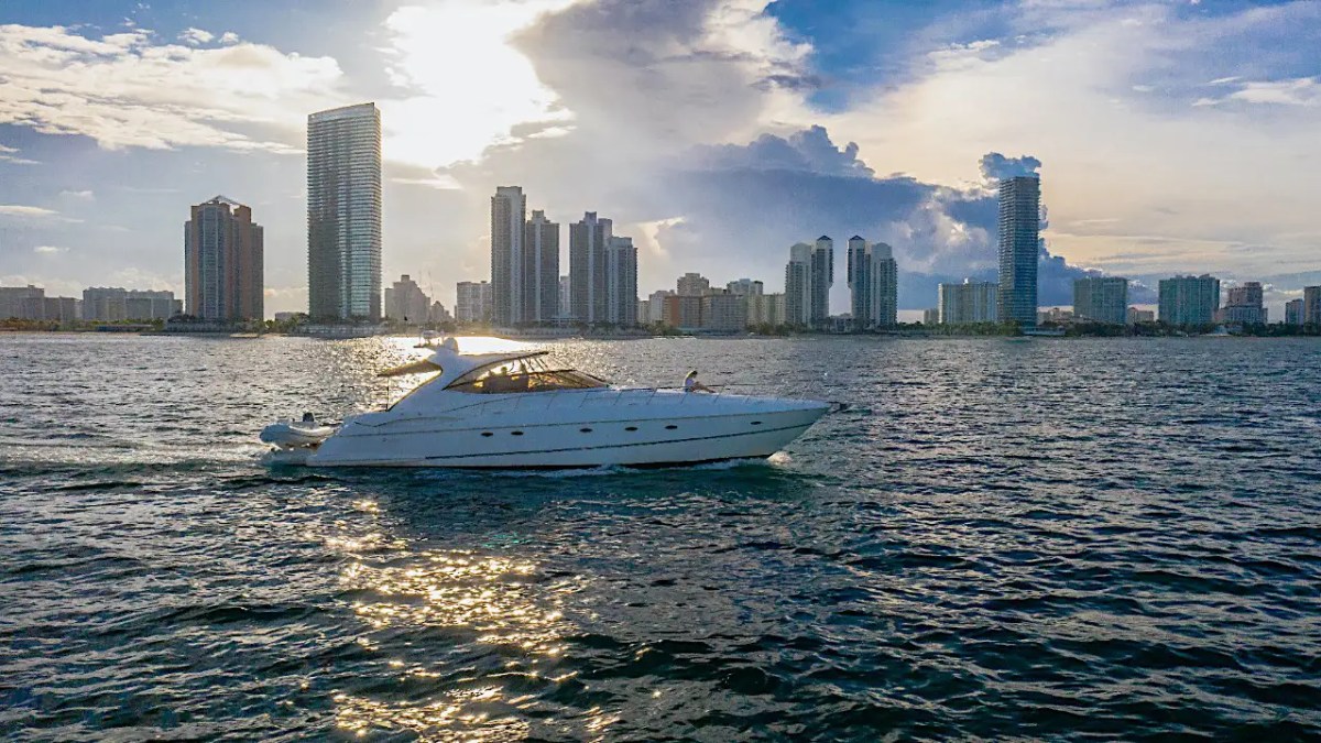 A luxury yacht sailing on water with a city skyline in the background at sunset.