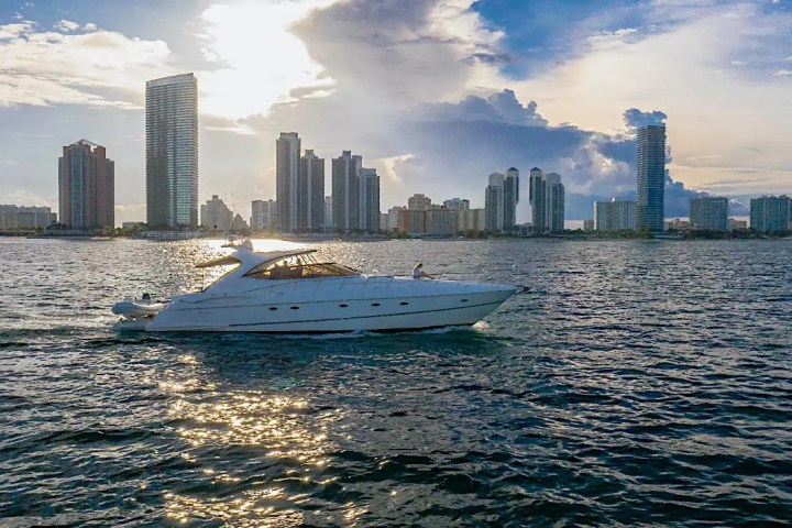A luxury yacht sailing on water with a city skyline in the background at sunset.