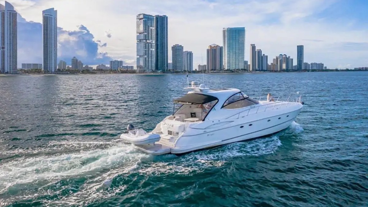 A white yacht cruising near a city skyline with tall buildings in the background on a sunny day.