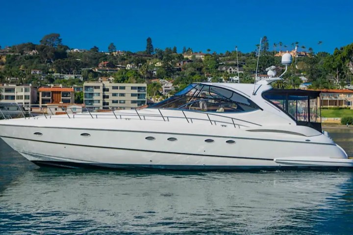 White yacht on calm water with a hillside town in the background under a clear blue sky.
