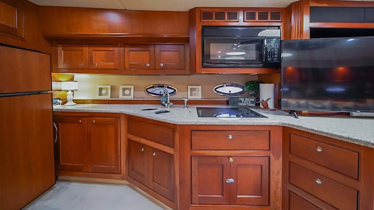 Wood-paneled yacht kitchen with microwave, TV, and countertops.