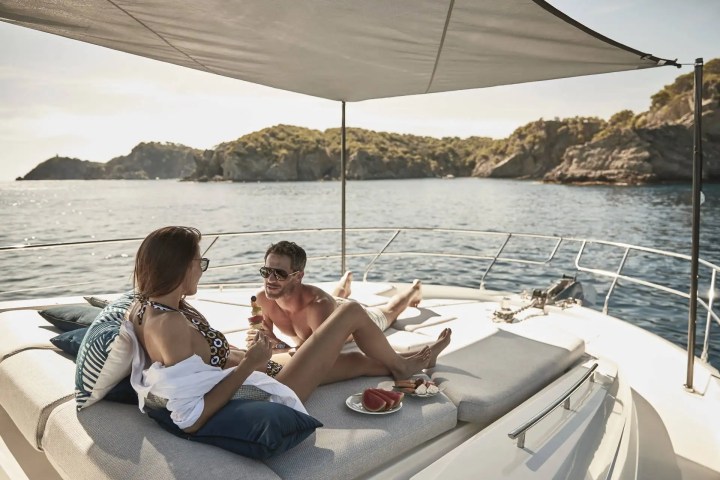 Two people relaxing on a yacht deck with snacks and scenic island view.