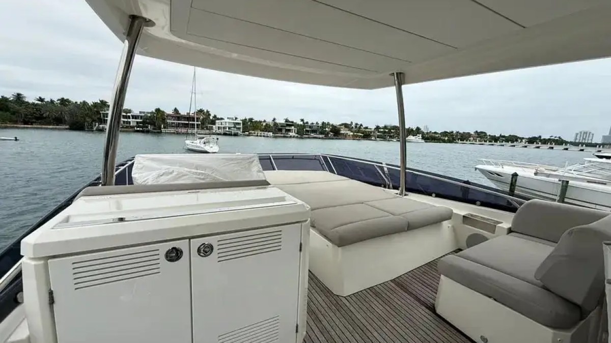 Upper deck of a yacht with seating, a cabinet, and ocean view.
