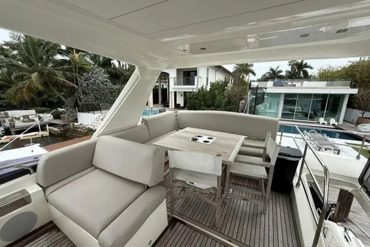 Boat deck with seating area and table, overlooking modern houses and palm trees.