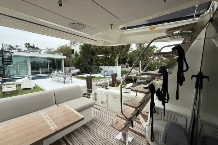 View from a yacht's deck with seating, facing a modern house and pool in the background.