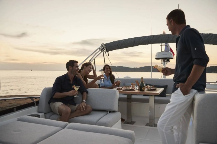 Four people on a boat enjoying drinks at sunset with a table of snacks.