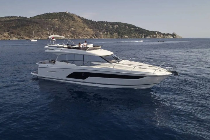 White yacht on calm sea with hilly coastline in background.