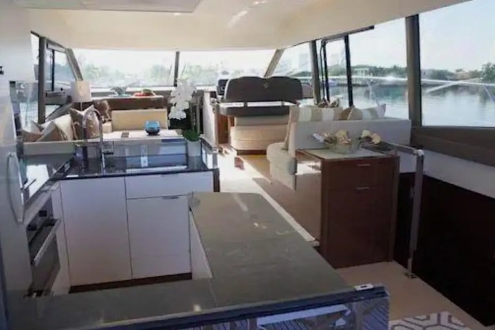 Interior of a yacht with a modern kitchen, seating area, and large windows overlooking water.