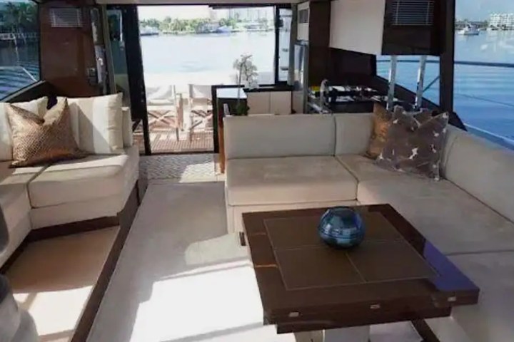 Luxurious yacht interior with beige sofas, a wooden table, and a view of water through large windows.