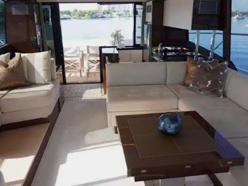 Luxurious yacht interior with beige sofas, a wooden table, and a view of water through large windows.