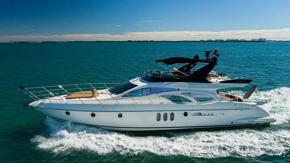 Luxury yacht cruising on calm blue sea under clear sky with distant cityscape.