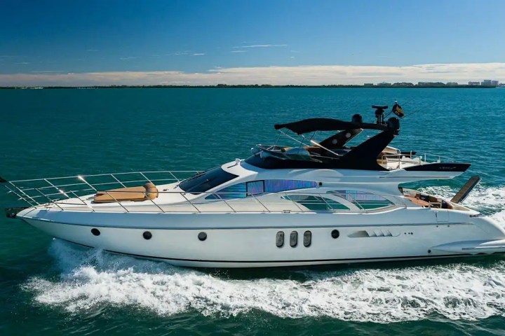 Luxury yacht cruising on calm blue sea under clear sky with distant cityscape.