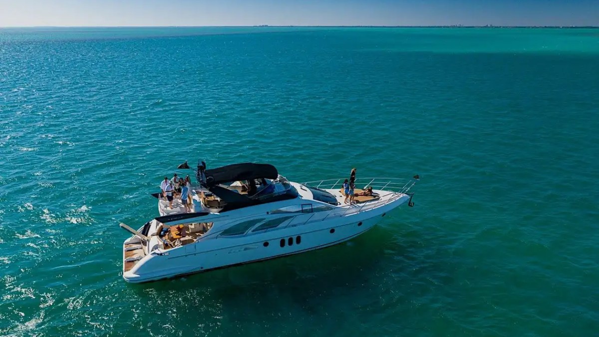 Aerial view of a yacht with people on a calm, blue ocean under a clear sky.