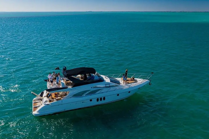 Aerial view of a yacht with people on a calm, blue ocean under a clear sky.
