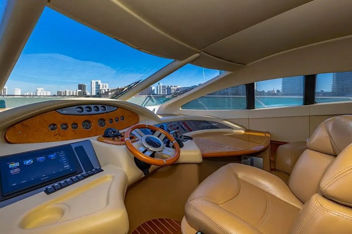 Luxurious yacht cockpit with leather seats, wood steering wheel, and city skyline view through windows.